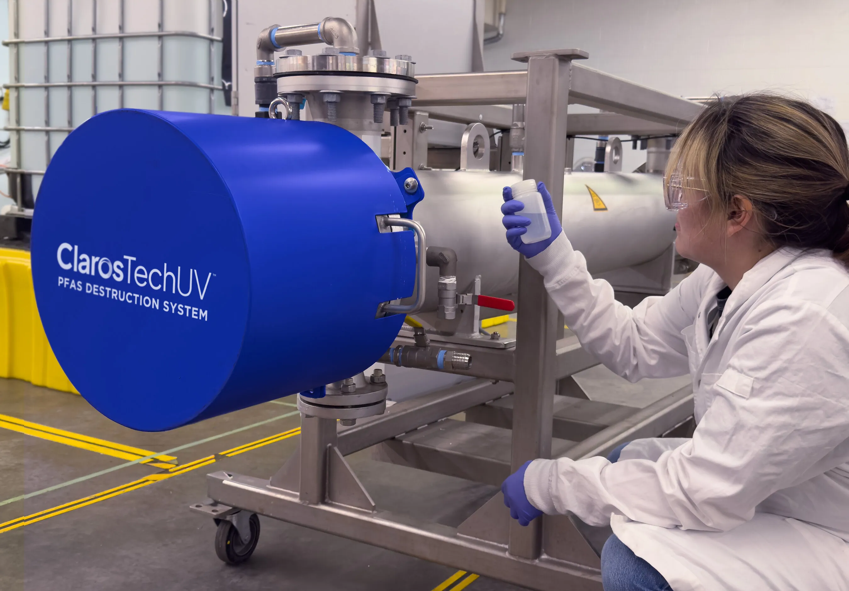 Lab worker holding a sample bottle beside a ClarosTechUV PFAS destruction system.
