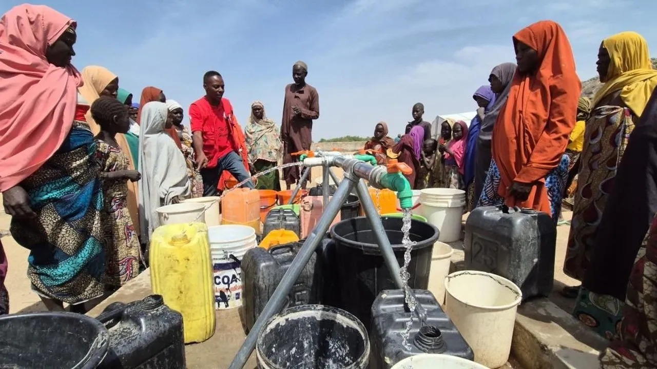 People gather around a water tap, filling buckets and jerry cans.